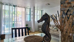 A living room with a glass coffee table, a decorative horse sculpture, a sofa, and a view of the outside through large windows with sheer curtains.