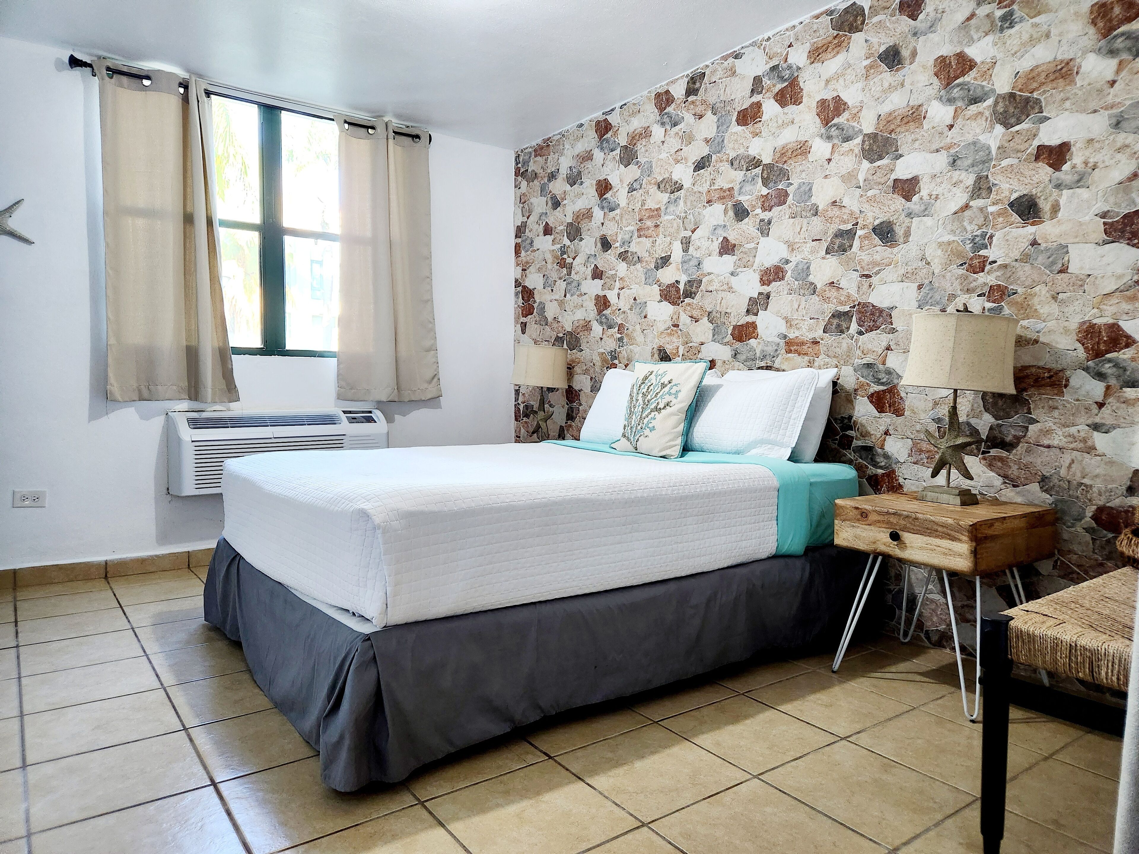 A neatly arranged bedroom with a bed, air conditioning unit, and a stone-patterned wall.