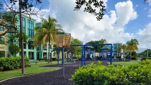 A playground with swings and climbing structures, surrounded by landscaped areas and palm trees.