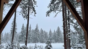 A snowy forest scene viewed through a wooden structure with snow-covered trees and a stone wall in the foreground. - Luxury Suncadia Retreat- Golf Course View, Fire Pit, Pool Table, Family-Friendly (Cle Elum)