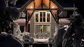 A snow-covered landscape with a wooden house featuring a large porch and a dining area. - Luxury Suncadia Retreat- Golf Course View, Fire Pit, Pool Table, Family-Friendly (Cle Elum)