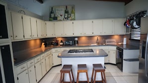 Una cocina con gabinetes blancos, encimera de granito, una isla integrada con taburetes y una cafetera.