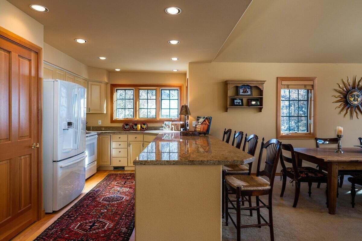 Una cocina con una isla central, armarios de madera, un refrigerador y un comedor con sillas y una mesa.