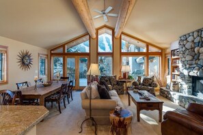 Un salon spacieux avec un haut plafond, de grandes fenêtres, une cheminée en pierre et un coin repas.