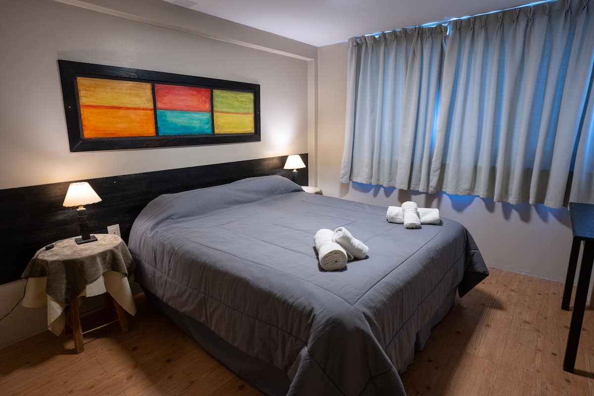 A hotel room with a large bed, two bedside tables with lamps, a painting on the wall, and a window with curtains.