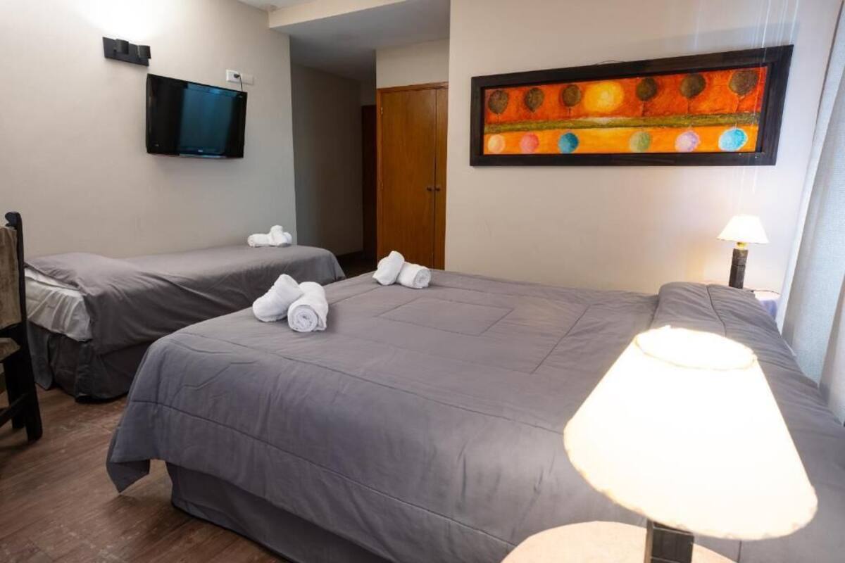 A hotel room with two beds, a TV, a painting, and a lamp.