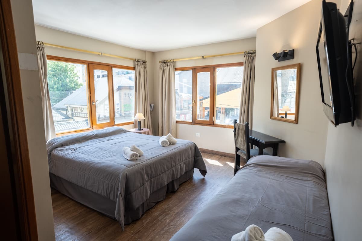 A hotel room with two beds, a desk, and large windows with curtains.