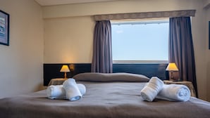 A hotel room with a large bed, two bedside lamps, a window with curtains, and two rolled towels on the bed. - Park Bariloche (San Carlos de Bariloche)