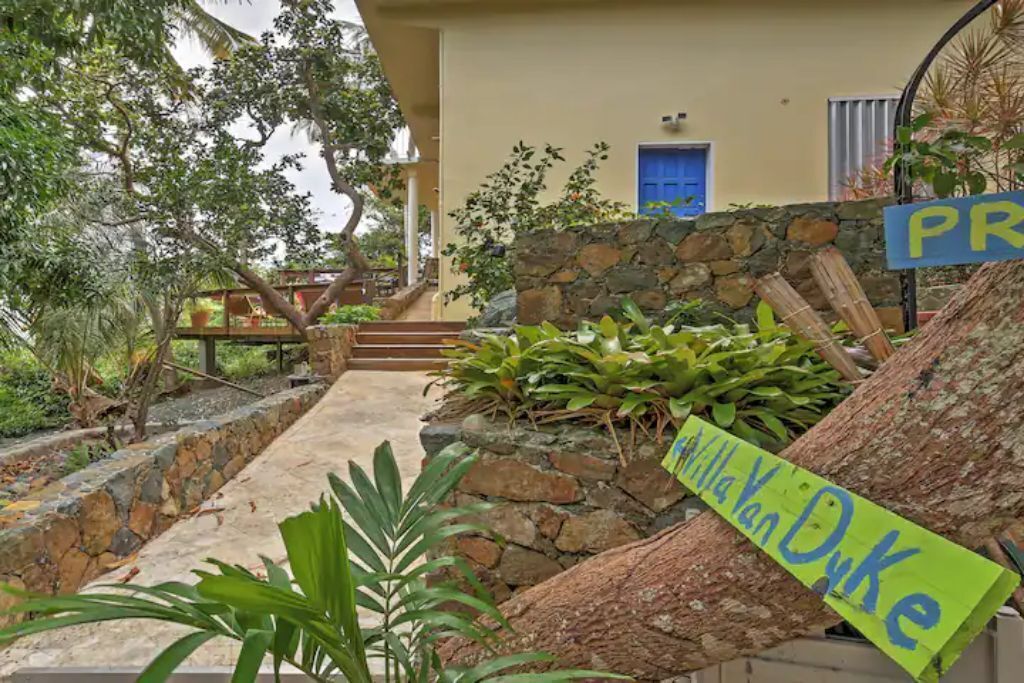 A stone pathway leading to a house with a blue door and a sign reading "Villa Van Duke".
