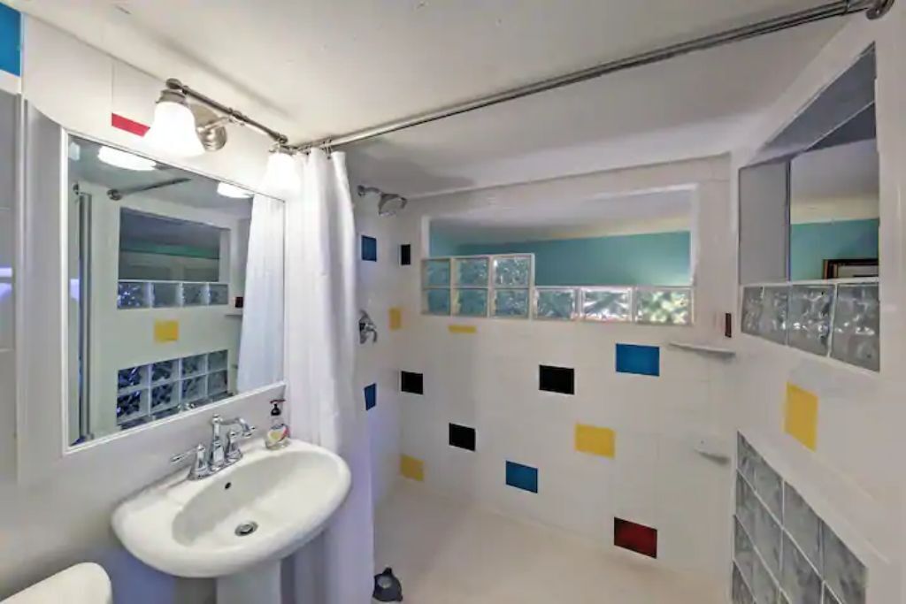 A bathroom with a white sink, a mirror, and a shower curtain. The walls are decorated with colorful square tiles.