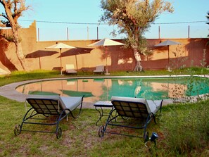 Una piscina con sillones de descanso y sombrillas, rodeada de césped y árboles.