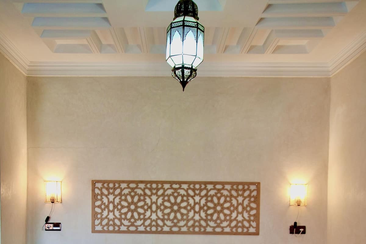 A hotel room with a large bed, a bench, a decorative wall panel, and two wall-mounted lights.