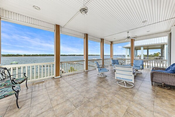 A covered outdoor area with a view of the water, featuring a seating area with chairs and a table, and a covered structure with a railing.