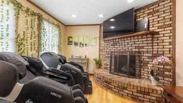 Ein Zimmer mit Massagesesseln, einem Kamin aus Ziegelsteinen und einem flachbildfernseher, der darüber angebracht ist.