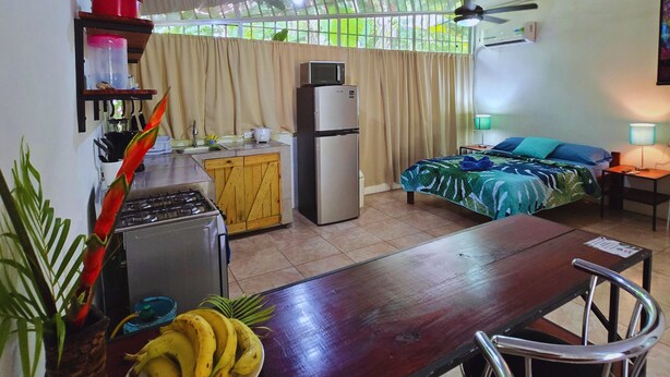 A compact room with a bed, a small kitchenette, a dining table, and a ceiling fan.
