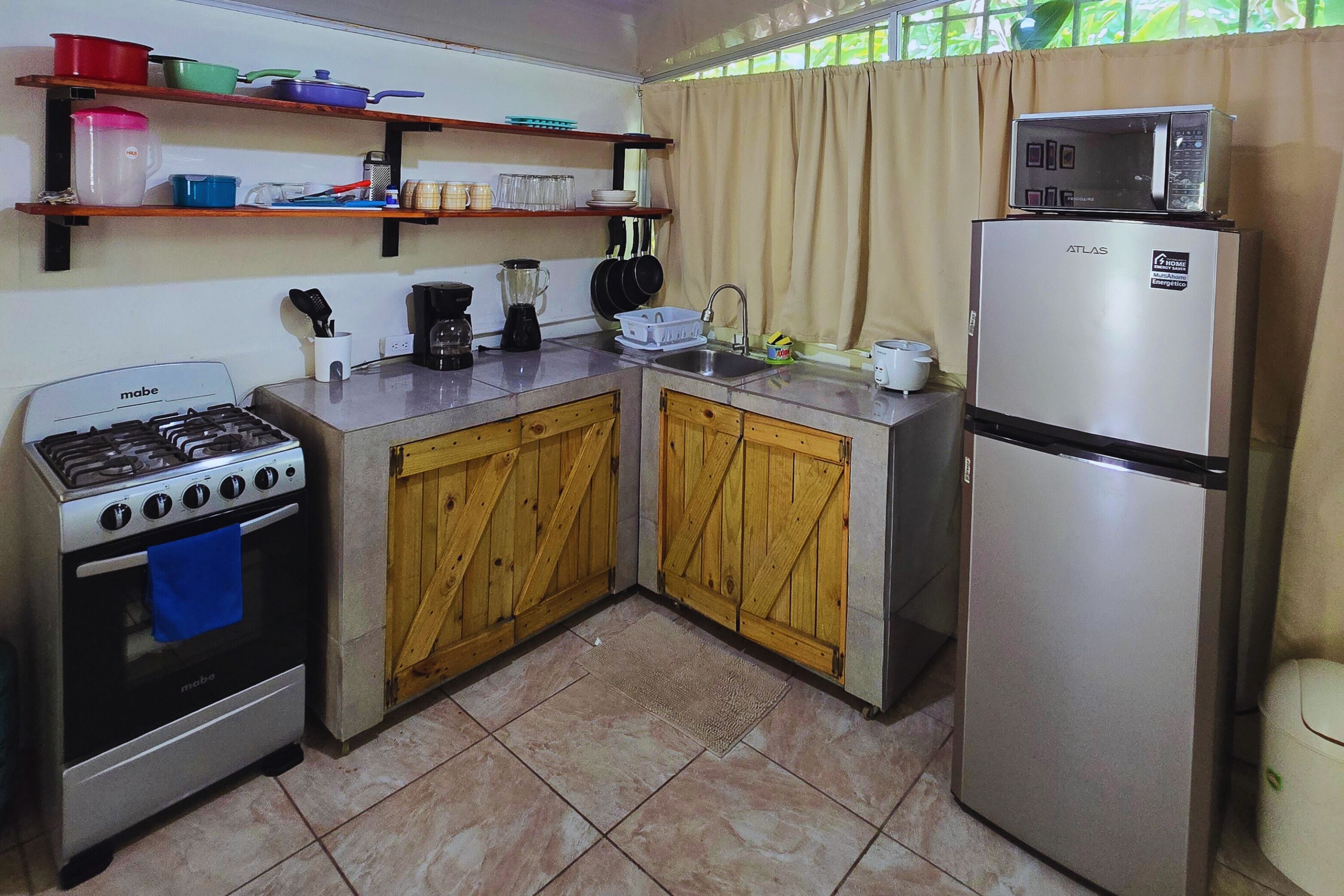 Uma cozinha compacta com fogão a gás, forno, armários de madeira, geladeira e micro-ondas em cima.