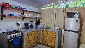 A compact kitchen with a gas stove, wooden cabinets, a refrigerator, and a window with curtains.