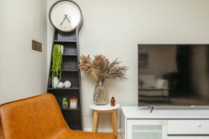 A living room with a sofa, a tall clock, a TV, and a small table with decorative items. - Spacious  newly redecorated 5BD Family Home (Eight Mile Plains)