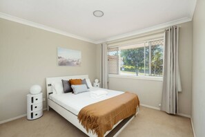 A bedroom with a bed, a nightstand, a window with curtains, and a painting on the wall. - Spacious  newly redecorated 5BD Family Home (Eight Mile Plains)