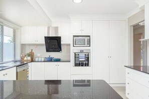 A modern kitchen with white cabinetry, a black countertop, and a built-in microwave and oven. - Spacious  newly redecorated 5BD Family Home (Eight Mile Plains)