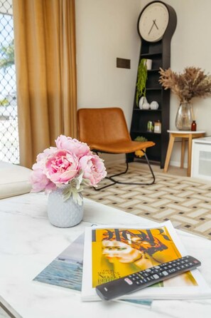 A living room with a sofa, a coffee table with a vase of flowers, a magazine, and a remote control. - Spacious  newly redecorated 5BD Family Home (Eight Mile Plains)