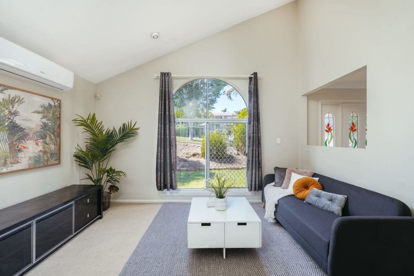 A modern living room with a sofa, a coffee table, and a large window with curtains.