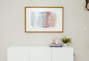 A framed abstract painting on a wall above a white console table with a plant and books. - Spacious  newly redecorated 5BD Family Home (Eight Mile Plains)