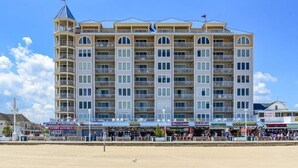 Un hôtel à plusieurs étages doté de balcons, situé en bord de mer et abritant divers commerces au rez-de-chaussée.