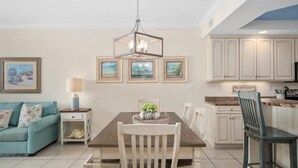 Un coin repas avec une table en bois, des chaises et un lustre. Des tableaux encadrés sont accrochés au mur au-dessus de la table.
