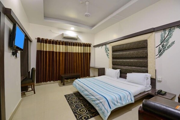 A hotel room with a bed, a desk, a chair, a television, and a window with curtains. - Hotel Mayura - Ambikapur (Ambikapur)