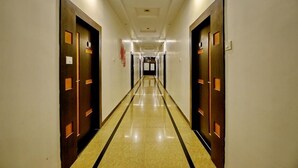 Een lange, smalle hotelgangen met deuren aan beide kanten, inbouwverlichting en een glanzende betegelde vloer.
