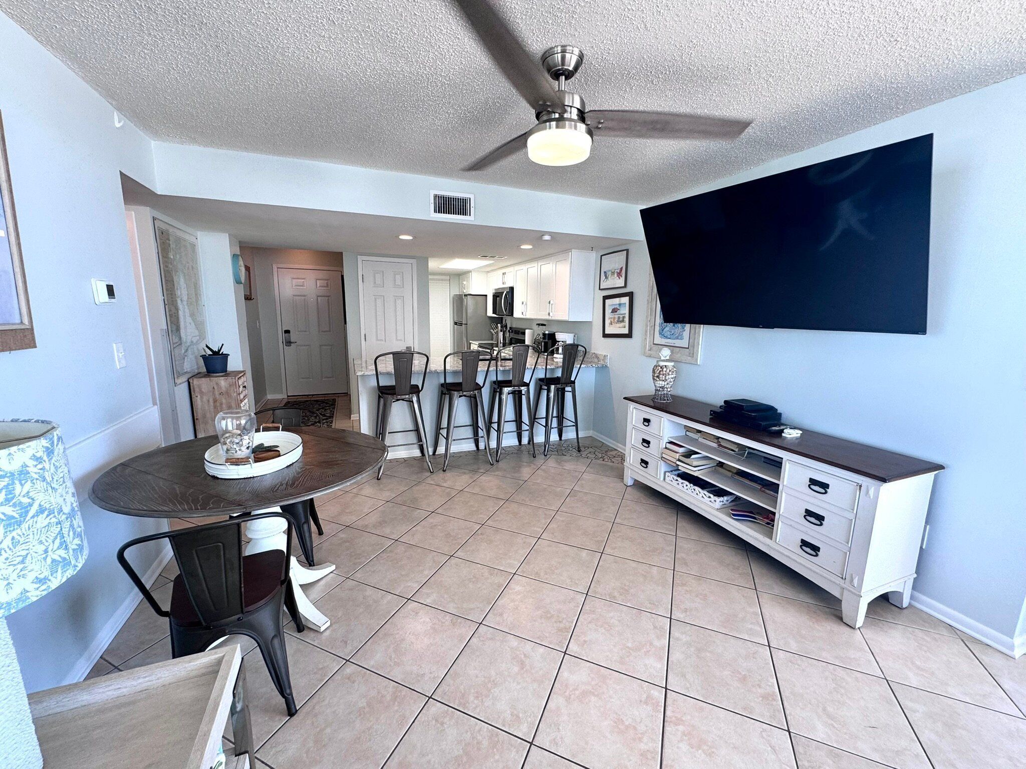 A modern kitchen with a dining area, a ceiling fan, and a TV mounted on the wall.
