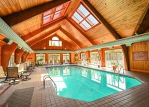 Une piscine intérieure dotée d’un haut plafond en bois et de grandes fenêtres.