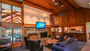 A cozy interior with a fireplace, a television, and a pool visible through large windows. - Summit View Townhouse 1mi to Mt Snow w/ Fireplace! (Dover)