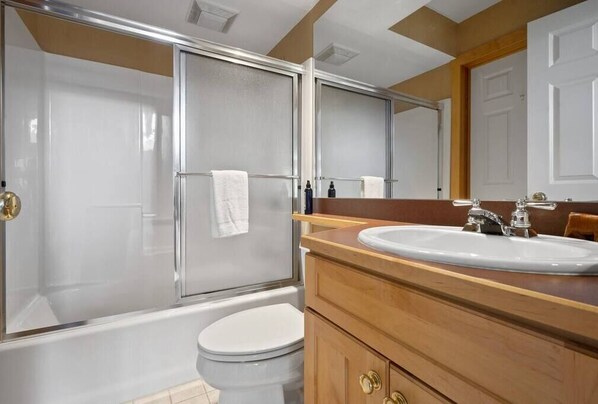 Une salle de bain avec une douche à parois de verre, des toilettes blanches, un meuble-lavabo en bois et un miroir.