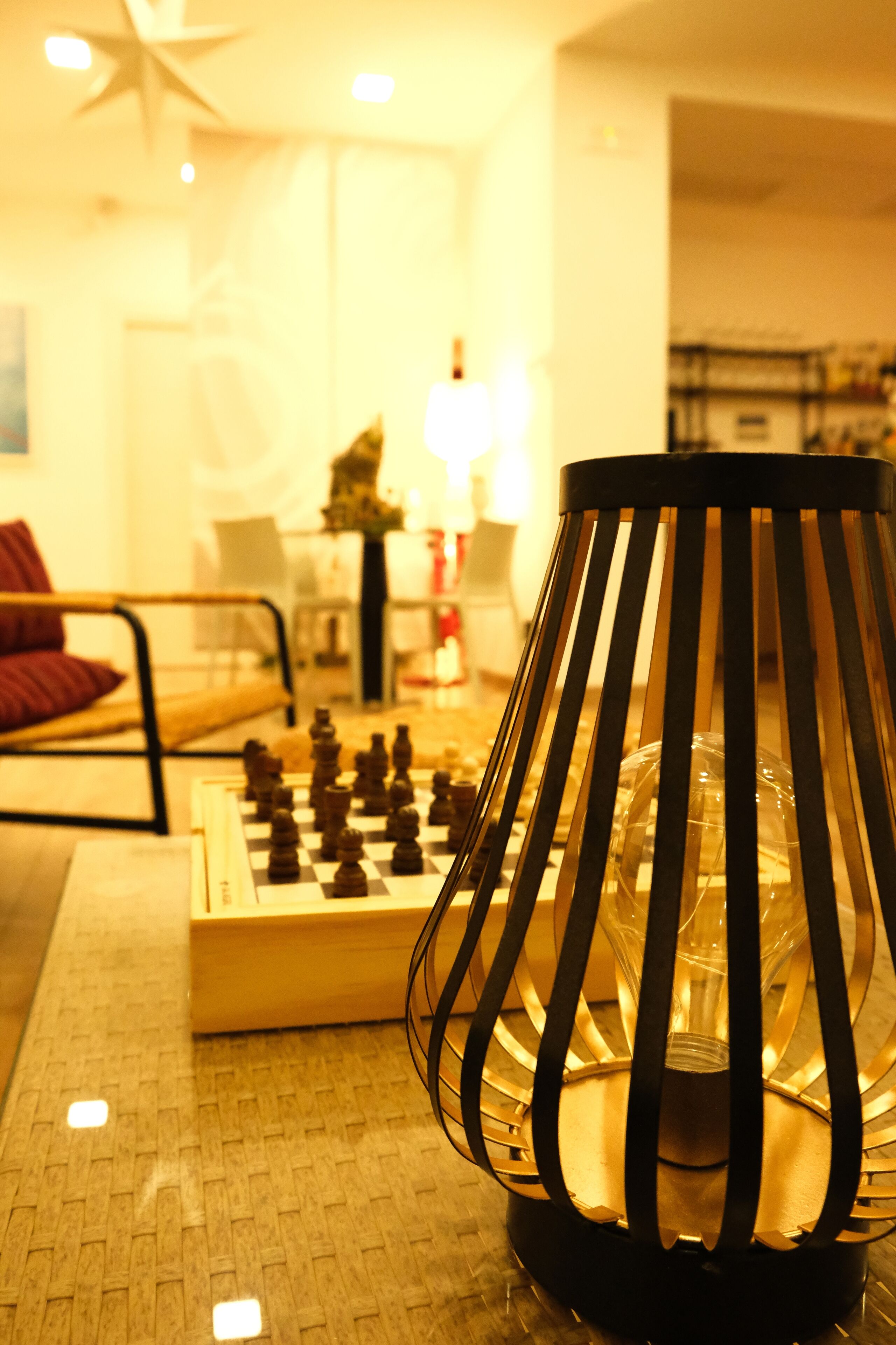 A chessboard on a table with a lamp in the foreground.