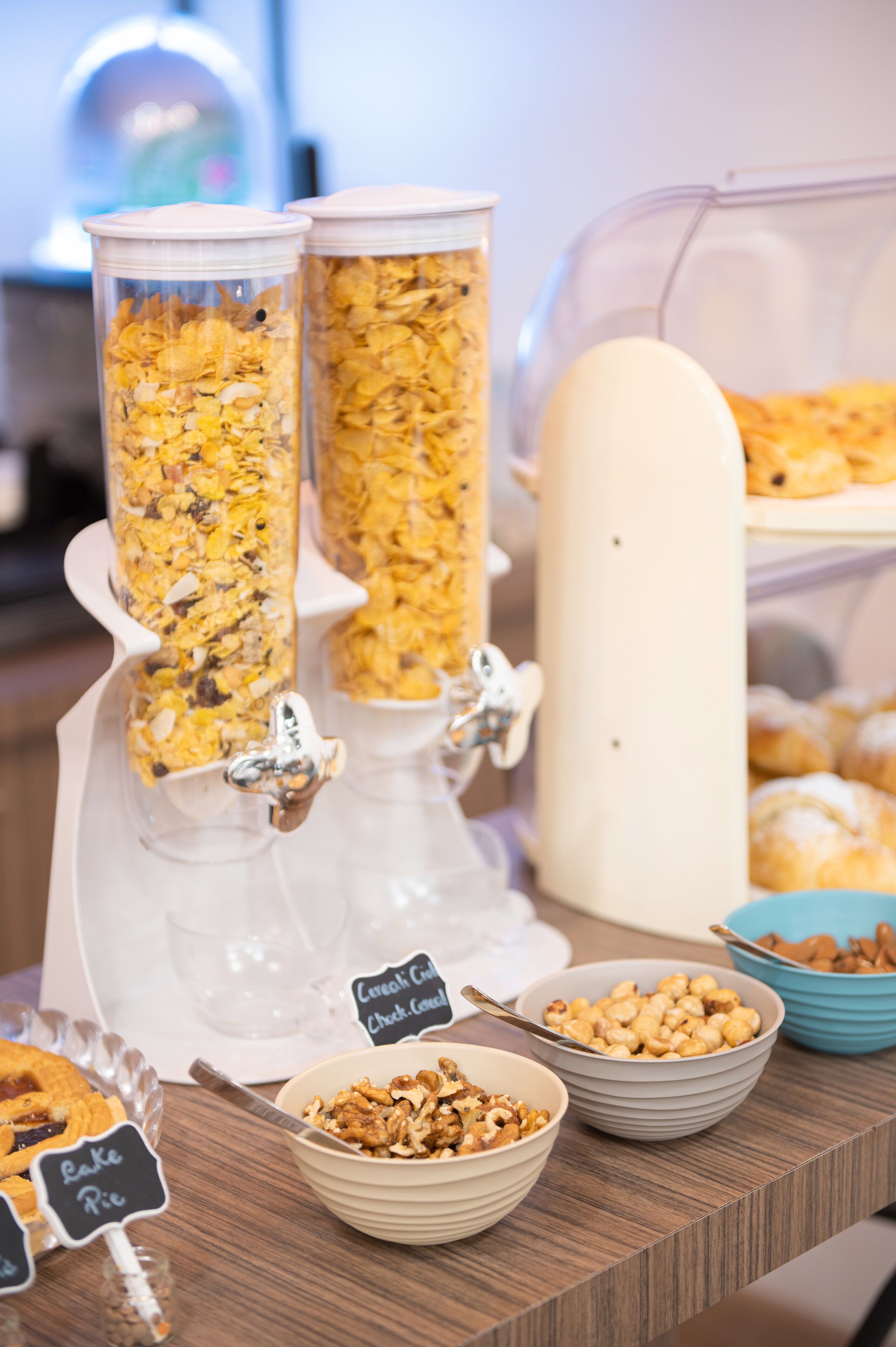 Montaje de bufé con dispensadores de cereales, tazones de cereal y una mesa de pasteles.