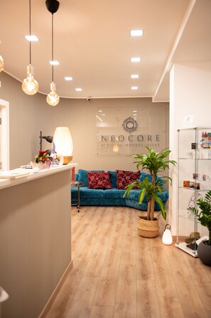 A reception area with a counter, a blue sofa, a potted plant, and a wall with the text "NEOCORE Discover, Wonder, Relax". - Neocore  (Naples)