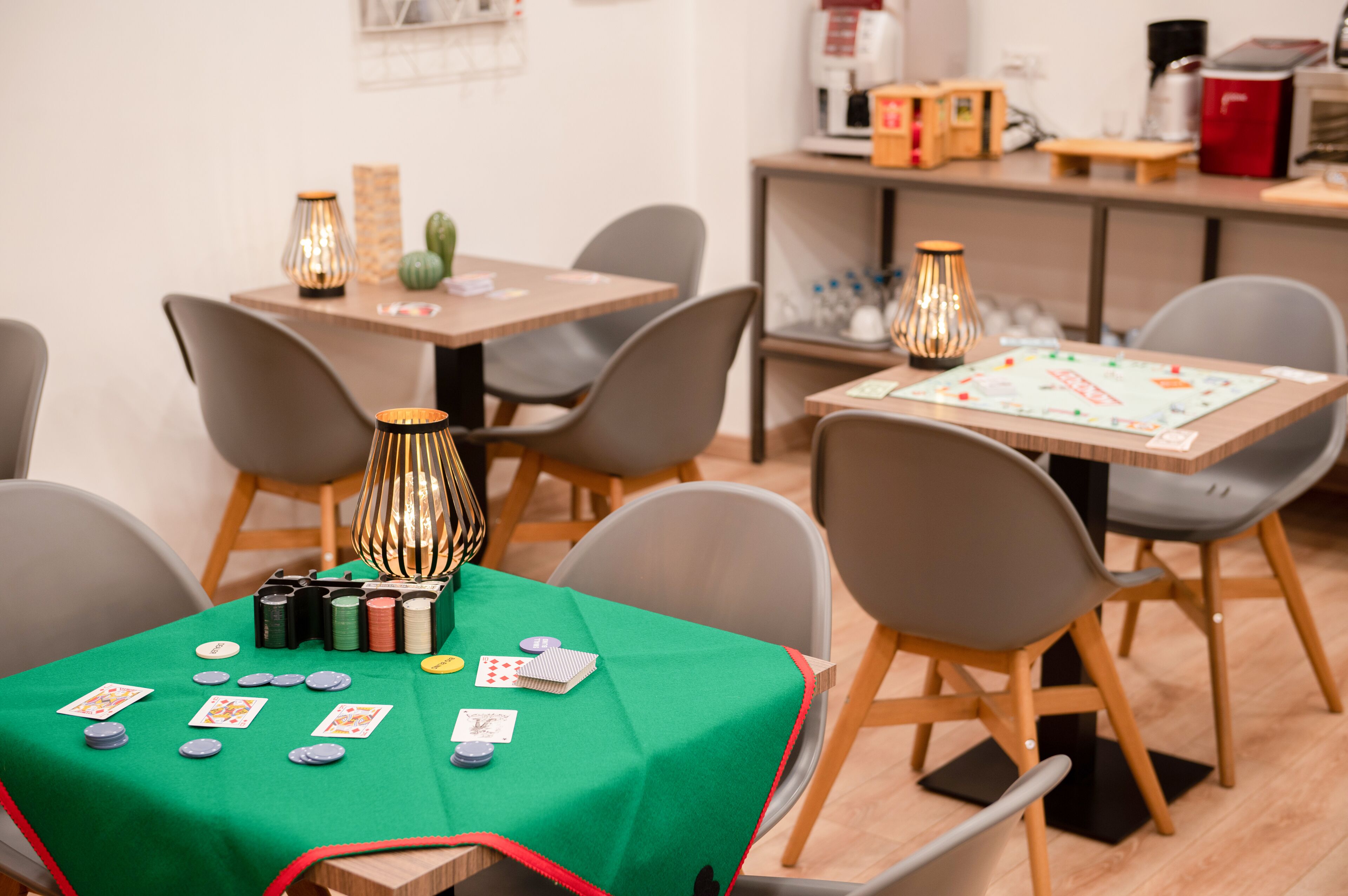 A room with a green table covered with playing cards and poker chips, a lamp, and a board game.