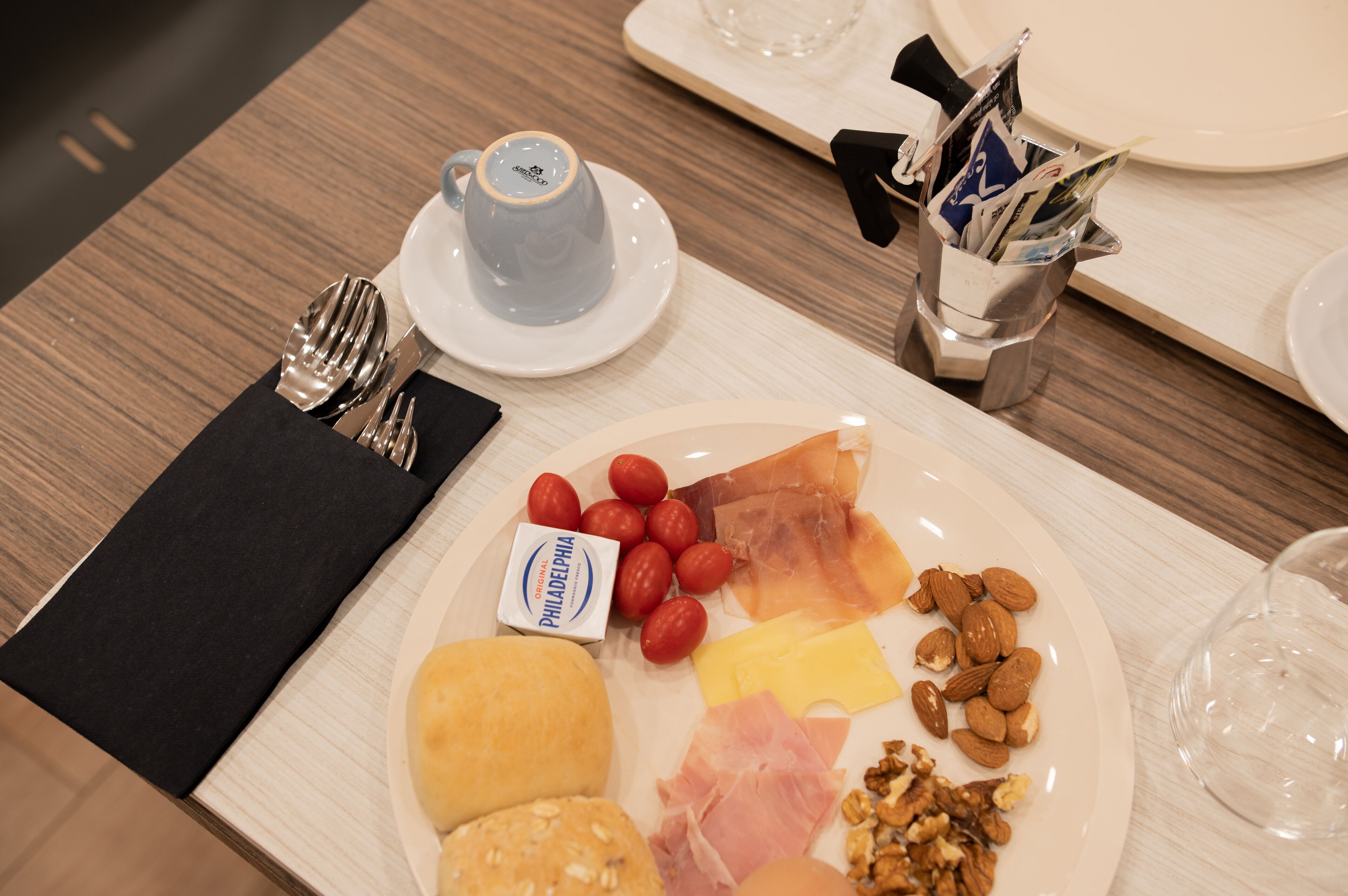 Een ontbijttafel met een bord verschillende kazen, fruit en noten, een koffiekop en een glas water.