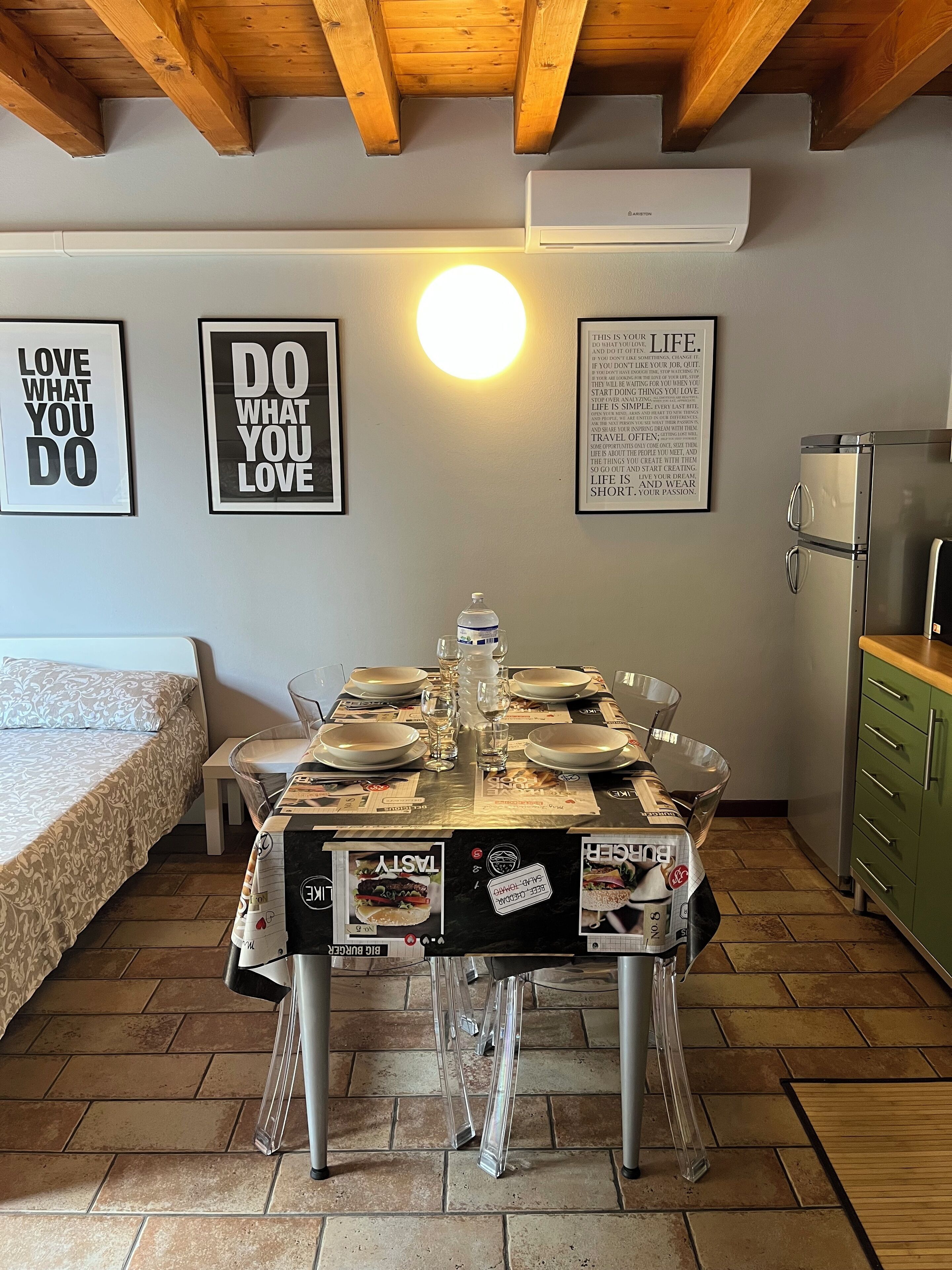 Una cocina compacta con una mesa de comedor para cuatro personas, una cama con ropa de cama estampada y decoración mural inspiradora.
