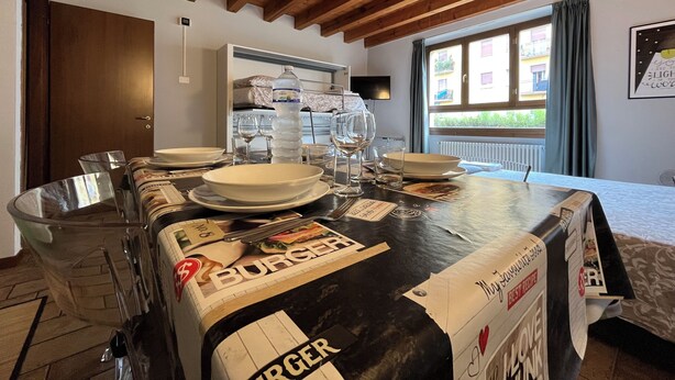 A dining area with a table set for two, a water bottle, wine glasses, and a burger box.