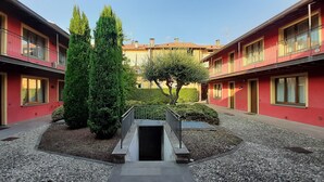 A courtyard with a central water feature, surrounded by red buildings with balconies and a well-maintained hedge.