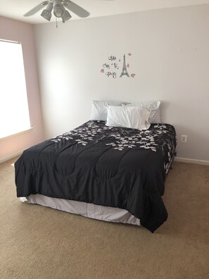 A bedroom with a bed, a ceiling fan, a wall decal of the Eiffel Tower, and a window.