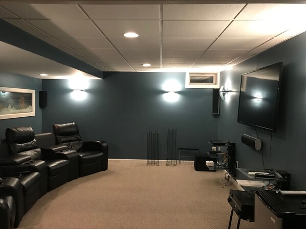 Una sala de cine en casa con una zona de asientos curvos, un televisor plano grande y piso alfombrado.