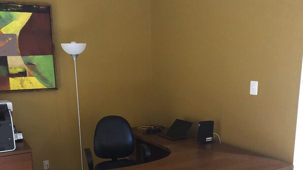 Une pièce avec un bureau en bois, un fauteuil de bureau noir, une lampe et un tableau accroché au mur.