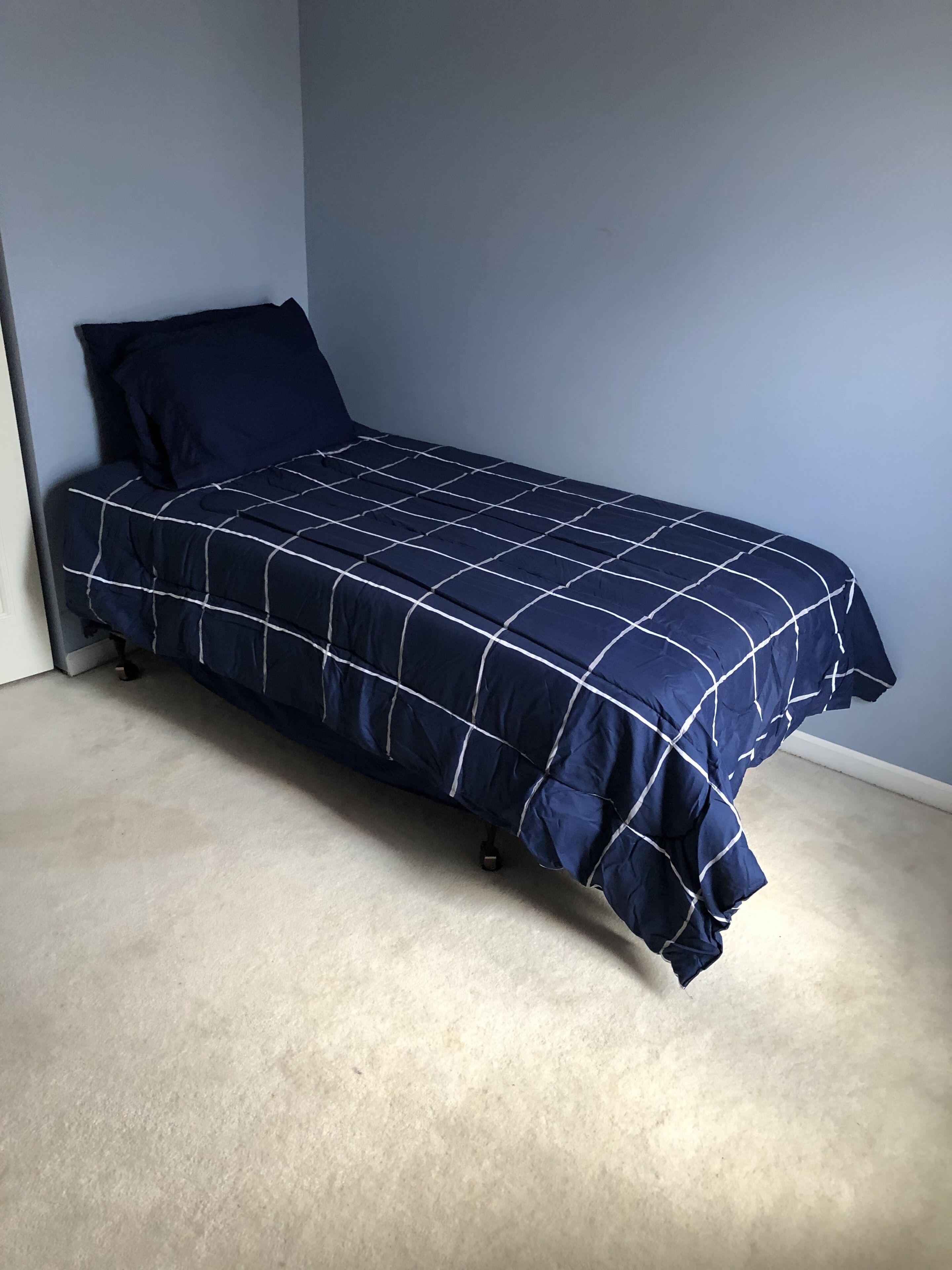 Ein Einzelbett mit einer dunkelblauen Steude in einem Zimmer mit hellblauen Wänden und einem hellen Teppich.