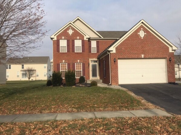 A two-story brick house with a garage, a front lawn, and a neighboring building.