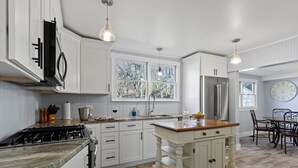 A kitchen with white cabinets, a central island, a stove, and a dining area with a table and chairs. - 1900 Farmhouse with Luxury Spa Bath, 2 Master Bedrooms, Historic Home (Whitwell)