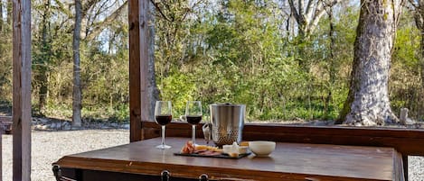 A wooden table set with a cheese platter, two glasses of red wine, a metal pitcher, and a bowl.